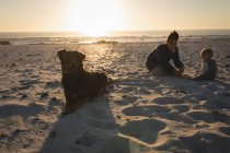 Mãe e filho relaxando na areia na praia durante o pôr do sol — Fotografia de Stock