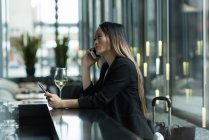 Mujer de negocios asiática hablando por teléfono mientras usa una tableta digital en el vestíbulo - foto de stock