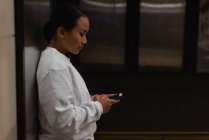 Mulher usando telefone celular na estação subterrânea — Fotografia de Stock