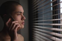 Молодой человек разговаривает по мобильному телефону, глядя в окно дома — стоковое фото