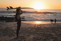 Surfista che trasporta tavola da surf sulla testa al crepuscolo — Foto stock