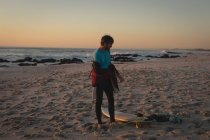 Prancha de surf removendo terno molhado na praia durante o pôr do sol — Fotografia de Stock
