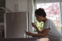 Frau frühstückt zu Hause mit Handy — Stockfoto