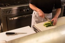Sección media del chef picando verduras en la cocina - foto de stock