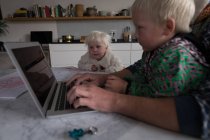 Père utilisant un ordinateur portable à la table avec fils et fille dans la cuisine à la maison
. — Photo de stock