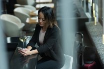 Азіатський бізнес-леді сидить сама, використовуючи свій мобільний телефон у фойє — стокове фото