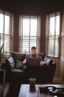 Чоловік сидить на дивані, використовуючи свій ноутбук у вітальні — стокове фото