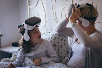Mãe e filha usando fone de ouvido realidade virtual na cama no quarto — Fotografia de Stock