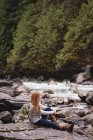 Mujer sentada en la costa del río en el bosque - foto de stock