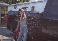 Mujer divirtiéndose mientras lava el coche garaje exterior - foto de stock