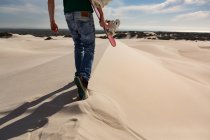 Mann läuft an einem sonnigen Tag mit Sandbrett in der Wüste — Stockfoto