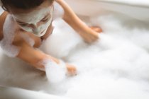 Frau mit Gesichtsmaske badet zu Hause mit Schaum, Nahaufnahme. — Stockfoto