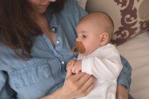 Niedliches Baby mit Schnuller im Mund liegt zu Hause im Arm der Mutter — Stockfoto