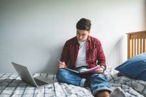Giovane uomo che studia sul letto con notebook e laptop a casa . — Foto stock