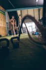 Homem musculoso determinado exercitando com corda no estúdio de fitness — Fotografia de Stock