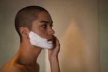 Молодой человек наносит крем для бритья на лицо в ванной комнате — стоковое фото