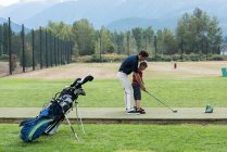 Father assisting his son to play golf in the course — Stock Photo