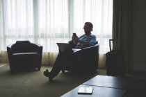 Бізнесмен, використовуючи мобільний телефон, сидячи на кріслі в готельному номері — стокове фото