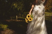 Rückansicht der Braut mit einem Sonnenblumenstrauß im Garten — Stockfoto