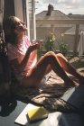 Frau sitzt in Balkonnähe, während sie zu Hause Kaffee trinkt und Musik hört. — Stockfoto