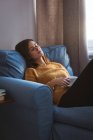 Junge Frau entspannt auf Sofa mit einer Tasse Kaffee im Wohnzimmer zu Hause — Stockfoto
