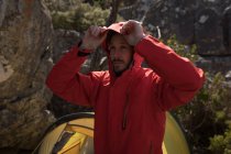 Escursionista in piedi vicino tenda mettere il berretto giacca in una giornata di sole — Foto stock
