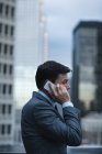 Вид збоку бізнесмена, який говорить на мобільному телефоні проти хмарочоса — стокове фото