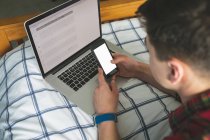 Man using mobile phone with laptop at bed, close-up. — Stock Photo