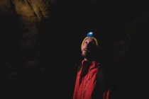 Турист, стоящий в темной пещере с фонариком на голове и рюкзаком — стоковое фото