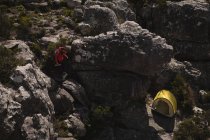 Hiker climbing down the rocks toward tent on a sunny day — Stock Photo