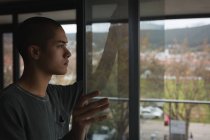 Задумчивый молодой человек смотрит в окно на дом — стоковое фото