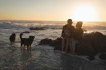 Famiglia rilassarsi sulla roccia in spiaggia durante il tramonto — Foto stock