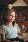 Linda chica con una corona que sostiene la calabaza en la cocina en casa - foto de stock