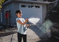 Boy washing car with a high pressure water jet outside garage — Stock Photo