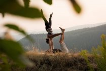 Sporty couple practicing acro yoga in a lush green ground at the time of dwan — Stock Photo