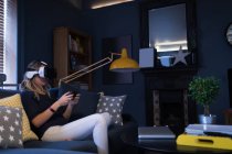 Frau sitzt auf Sofa und benutzt ihr Virtual-Reality-Headset zu Hause — Stockfoto