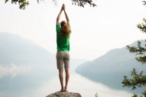 Fit man performing stretching exercise on the edge of a rock at the time of dawn — Stock Photo