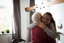 Sonriendo abuela y nieta abrazándose en la sala de estar - foto de stock