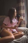 Ragazza adolescente che beve caffè freddo sul divano, tenendo lo smartphone e guardando lontano a casa . — Foto stock