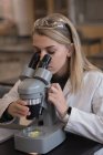 Дівчина-підліток експериментує на мікроскопі в лабораторії в університеті — стокове фото