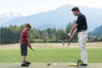 Отец помогает сыну играть в гольф на поле — стоковое фото