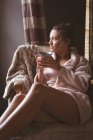Nachdenkliche Frau beim Kaffee im Sessel zu Hause. — Stockfoto