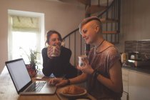 Casal de lésbicas usando laptop enquanto toma café em casa . — Fotografia de Stock