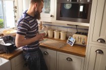 Чоловік дивиться на планшет, маючи каву на кухні — стокове фото