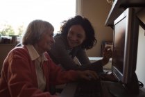 Hausmeister hilft Seniorin beim Arbeiten am Computer im Schwesternzimmer — Stockfoto