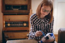 Carino ragazza in occhiali fissaggio il robot giocattolo a casa — Foto stock