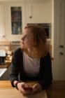 Frau schaut weg, während sie zu Hause ihr Handy in der Küche benutzt — Stockfoto
