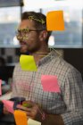 Thoughtful male executive reading sticky notes on glass wall in office. — Stock Photo