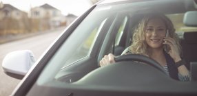 Улыбающаяся исполнительная женщина разговаривает по мобильному телефону за рулем автомобиля — стоковое фото