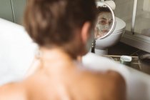 Frau trägt Gesichtsmaske in Badewanne vor Spiegel zu Hause auf. — Stockfoto